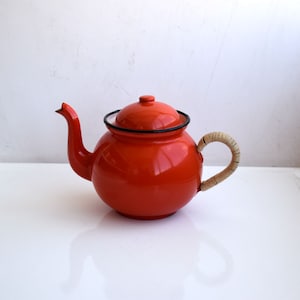 May include: A bright orange enamel teapot with a black rim and a woven rope handle.