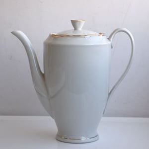 Könnte beinhalten: Weiße Porzellan-Kaffeekanne mit goldener Verzierung um Deckel und Boden. Die Kanne hat einen runden Korpus und einen Ausguss an der Seite.
