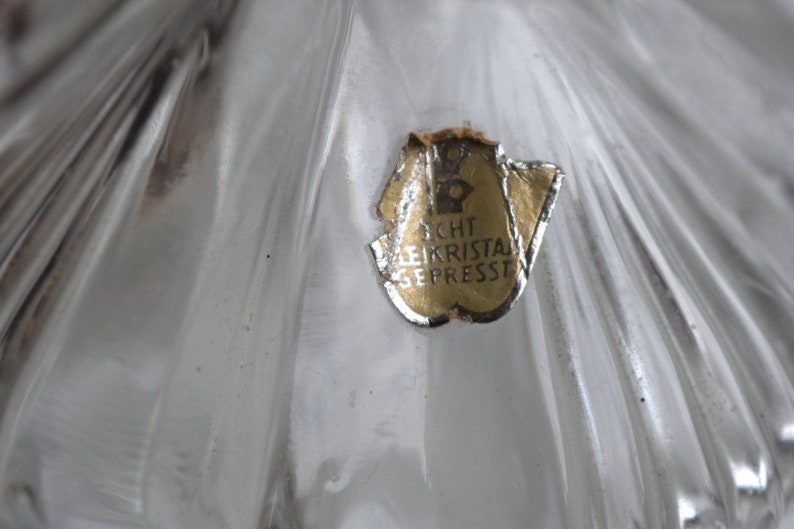 May include: Close-up of a clear glass object with a gold label that reads "Echt Bleikristal Gepresst".