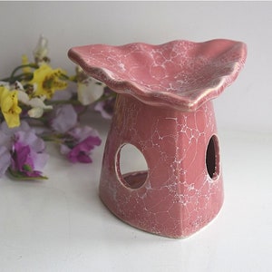 Può includere: Un bruciatore per oli essenziali in ceramica rosa con un bordo a forma di conchiglia e una glassa screpolata. Il bruciatore ha due fori laterali per la ventilazione.