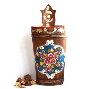 May include: A wooden bucket with a floral design painted on the side. The bucket is brown with blue, red, yellow, and white paint. The bucket has a handle on the top.