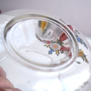 K&ouml;nnte beinhalten: Eine klare Glassch&uuml;ssel mit einem floralen Design, das auf der Au&szlig;enseite bemalt ist. Das Design zeigt rote, gelbe, blaue und gr&uuml;ne Blumen.