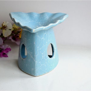 May include: A light blue ceramic oil burner with a scalloped top and three open holes. The burner has a crackled glaze finish.