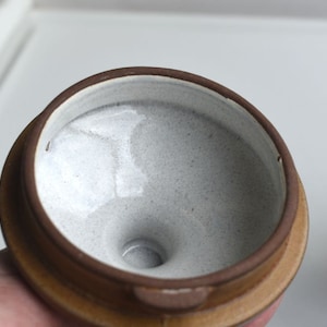 Może przedstawiać: Zbliżenie wnętrza brązowego garnka ceramicznego z białą glazurą. Garnek ma okrągły otw&oacute;r i mały otw&oacute;r w środku.