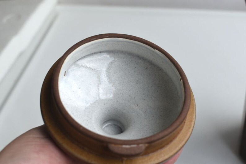 Może przedstawiać: Zbliżenie wnętrza brązowego garnka ceramicznego z białą glazurą. Garnek ma okrągły otw&oacute;r i mały otw&oacute;r w środku.