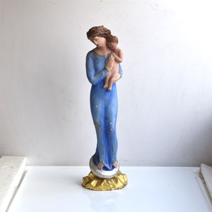 Op de afbeelding: Een blauw geverfd beeldje van de Maagd Maria die een baby Jezus vasthoudt. Het beeldje staat op een gouden voet.