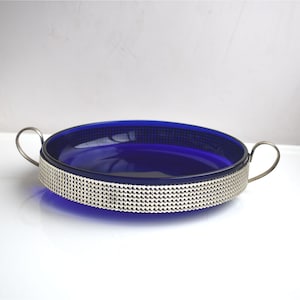 Op de afbeelding: Een serveerschaal van kobaltblauw glas met zilveren metalen handvatten en een decoratieve zilveren band rond de rand.