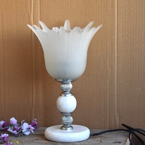 May include: A white frosted glass table lamp with a flower-shaped shade and a silver base with a white marble base.