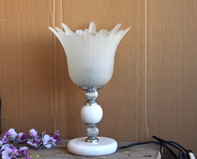 May include: A white frosted glass table lamp with a flower-shaped shade and a silver base with a white marble base.