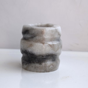 May include: A small, white marble vase with black marbling. The vase has a rounded, cylindrical shape with a slightly flared top.