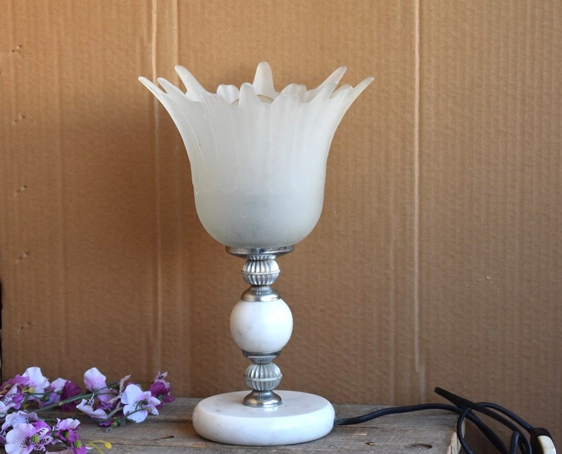 May include: A white frosted glass table lamp with a flower-shaped shade and a silver base with a white marble base.