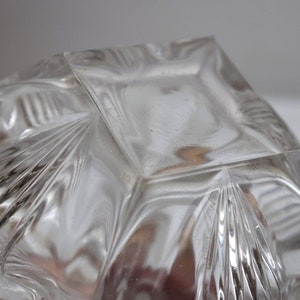 May include: Clear glass bowl with a square base and a decorative, geometric pattern. The bowl has a scalloped edge and a textured surface.
