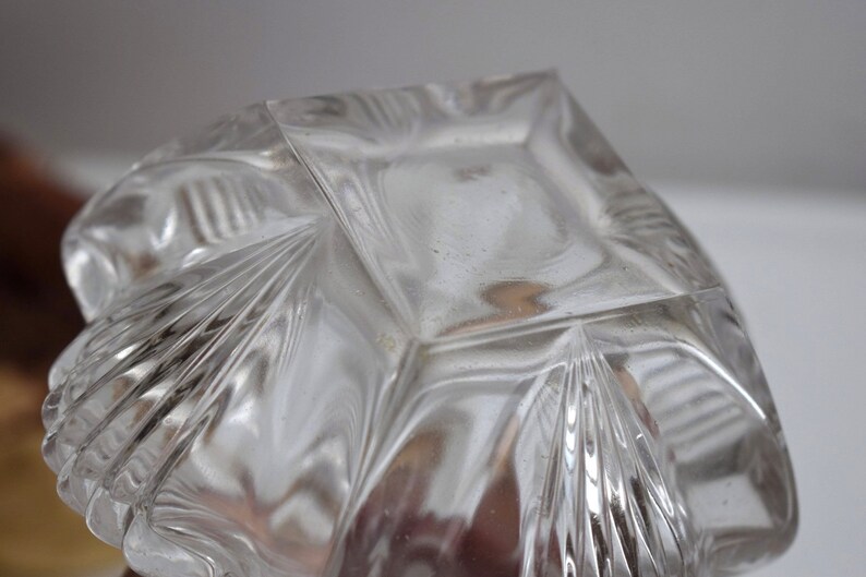 May include: Clear glass bowl with a square base and a decorative, geometric pattern. The bowl has a scalloped edge and a textured surface.