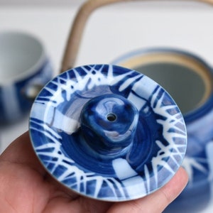 Puede incluir: Tapa de tetera de cer&aacute;mica azul y blanca con un dise&ntilde;o estampado en blanco y azul. La tapa tiene un peque&ntilde;o agujero en el centro.