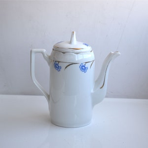 Puede incluir: Tetera de cerámica blanca con ribete dorado y diseño floral azul.
