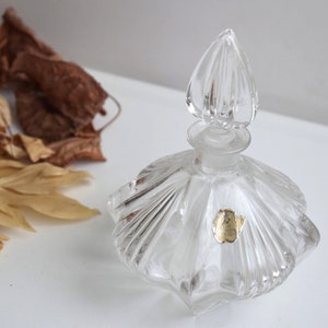 May include: A clear glass perfume bottle with a faceted design and a decorative stopper. The bottle has a gold label with the text "Made in Italy".