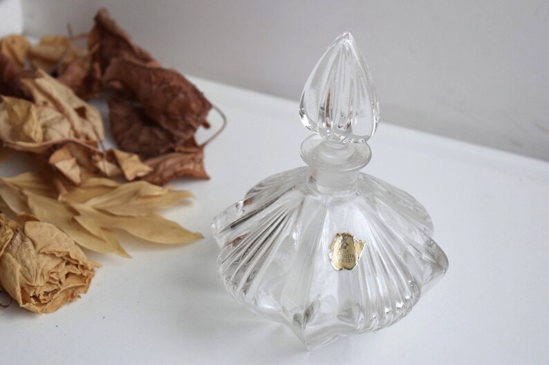 May include: A clear glass perfume bottle with a faceted design and a decorative stopper. The bottle has a gold label with the text "Made in Italy".