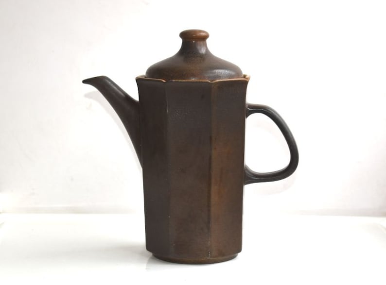 Może przedstawiać: Brązowy ceramiczny czajnik z pokrywką i uchwytem. Czajnik ma geometryczny kształt z ośmioma bokami.