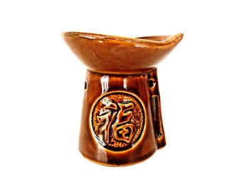 May include: A brown ceramic oil burner with a wide, shallow top and a round base. The burner features a raised, circular design with the Chinese character for "fortune" in the center.