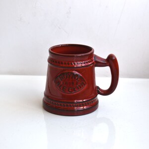Peut inclure: Une chope à bière en céramique rouge avec un motif en relief et les mots "Royal Ale Club" sur le devant.
