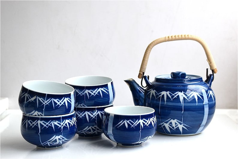 Puede incluir: Un juego de t&eacute; azul y blanco con una tetera y cuatro tazas. La tetera tiene un dise&ntilde;o de bamb&uacute; y un asa tejida. Las tazas est&aacute;n apiladas una encima de la otra.