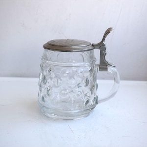 May include: A clear glass beer stein with a pewter lid and handle. The stein has a textured, bubble-like design.