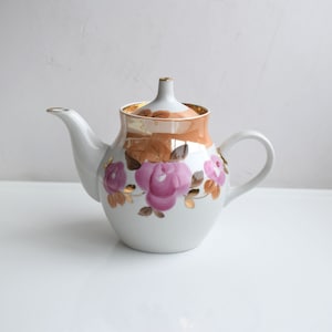 May include: White porcelain teapot with a floral design featuring pink roses and gold accents. The teapot has a round body and a curved spout.