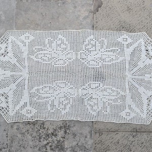 May include: A white crocheted table runner with a delicate floral pattern. The runner has a scalloped edge and is made of fine yarn.