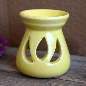 May include: A yellow ceramic oil burner with a decorative cut-out design. The burner has a wide, shallow top for holding essential oils or wax melts.