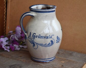 May include: A white ceramic pitcher with blue and white floral designs and the text "Grünwald" on the side.