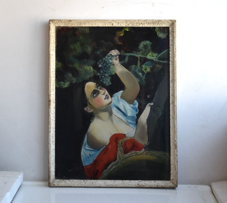 May include: A vintage oil painting on canvas depicting a woman reaching for a bunch of grapes in a vineyard. The woman is wearing a blue and white dress and a red shawl. The painting is framed in a white frame.