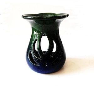 May include: A blue and green ceramic oil burner with a decorative cutout design. The burner has a wide, flat top and a rounded base.