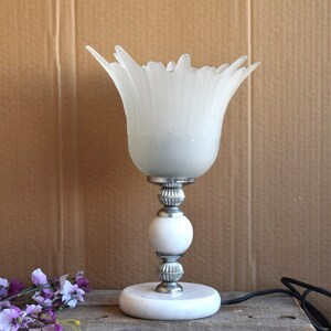 May include: A white table lamp with a frosted glass shade shaped like a flower. The lamp has a silver base with a white marble base.