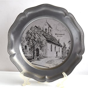 May include: A silver pewter plate with a black and white image of a church with the text "Weisweil Kirche" on the plate.