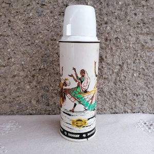 Könnte beinhalten: Weiße Thermoskanne mit einer bunten Illustration von Tänzern in traditioneller indischer Kleidung. Die Thermoskanne hat einen weißen Deckel und ein schwarzes Band um den Boden mit dem aufgedruckten Text "Made in Germany".