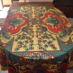 May include: A round tablecloth with a green, red, and gold floral pattern. The tablecloth has a damask-like texture and features a repeating design of stylized flowers and leaves.