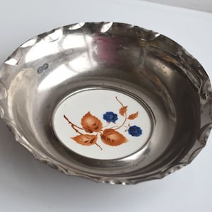 May include: A silver bowl with a white ceramic insert featuring a brown floral design with blue berries.