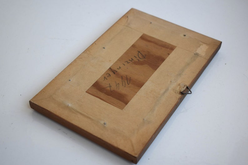 K&ouml;nnte beinhalten: Die R&uuml;ckseite eines Holzbildrahmens mit einer handschriftlichen Inschrift, die "H.H. Dirszu, N.Y." lautet.