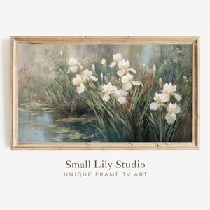 May include: A framed painting of white irises growing near a pond. The artwork has a vintage aesthetic, with soft colors and a naturalistic style. The frame is a light brown color. The text "Small Lily Studio UNIQUE FRAME TV ART" is at the bottom.