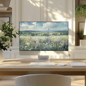 May include: A modern computer setup on a light wood desk. The computer displays a landscape painting of a field with wildflowers under a blue sky. A white keyboard, mouse, and a notepad are also on the desk. A white vase with flowers is on the left.