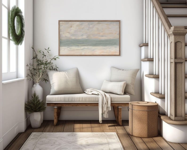K&ouml;nnte beinhalten: Ein gem&uuml;tliches Interieur mit einer Holzbank, cremefarbenen Kissen und einer Decke. Dar&uuml;ber h&auml;ngt ein gerahmtes Landschaftsbild in ged&auml;mpften T&ouml;nen. Ein gr&uuml;ner Kranz schm&uuml;ckt ein Fenster, und ein dekorativer Korb steht daneben.