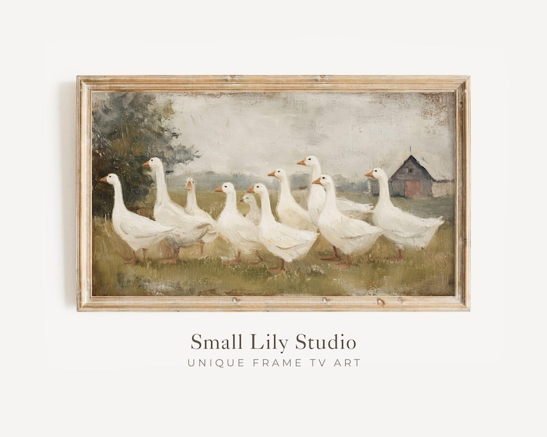 May include: A framed vintage-style painting depicts a flock of white geese walking across a grassy field. A barn is visible in the background. The artwork is set in a light brown wooden frame, evoking a rustic, pastoral theme.