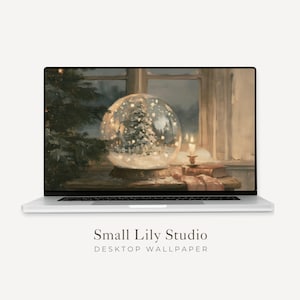 Puede incluir: Un portátil plateado que muestra una obra de arte digital de una bola de nieve con un árbol de Navidad, sobre una mesa con una vela y libros cerca de una ventana. El texto bajo la pantalla dice Small Lily Studio DESKTOP WALLPAPER.