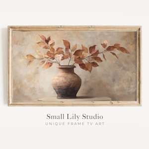 May include: A framed print featuring a still life of a brown vase with autumn leaves. The vase is a dark brown with a lighter brown rim. The leaves are a mix of orange and brown. The background is a soft, neutral color.
