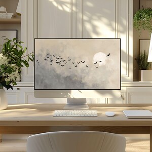 May include: A modern computer monitor displays a serene landscape with a full moon and silhouetted birds against a cloudy sky. The monitor sits on a light wood desk with a keyboard, mouse, and a white notepad. A white vase with flowers is on the left.