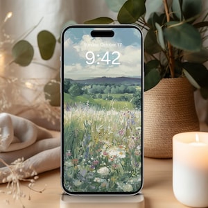 May include: A smartphone displays a landscape painting of a field with wildflowers under a cloudy sky. The time is 9:42 AM on Sunday, October 17. A lit candle and a potted plant are in the background.