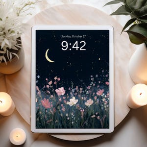 May include: A white tablet displays a floral wallpaper with a night sky, moon, and stars. The time is 9:42 on Sunday, October 17. The tablet rests on a wooden tray, surrounded by candles and plants in white vases.