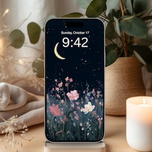 May include: A smartphone displays a floral wallpaper with a night sky, moon, and stars. The time is 9:42 AM on Sunday, October 17. A lit candle and a potted plant are in the background, creating a cozy atmosphere.