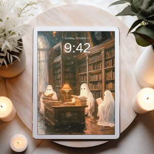 May include: A white tablet displays a spooky library scene with ghost figures reading books. The time is 9:42 on Sunday, October 17. The tablet is surrounded by lit candles, a white vase, and a potted plant on a marble surface.
