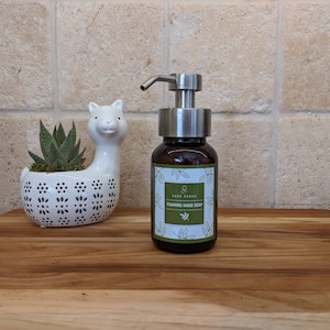 May include: A brown glass bottle with a silver pump dispenser filled with foaming hand soap. The bottle has a white label with green leaves and the text "Soap Sense Foaming Hand Soap".
